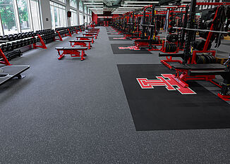 View of the side of the Texas Tech Olympic room that features free weights and benches, as well as weight racks.