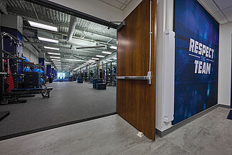 View of the Tennessee Titans Practice Facility, featuring the wooden door leading into the weight room, with Thunder Gray REGUPOL aktivpro roll flooring and white walls.